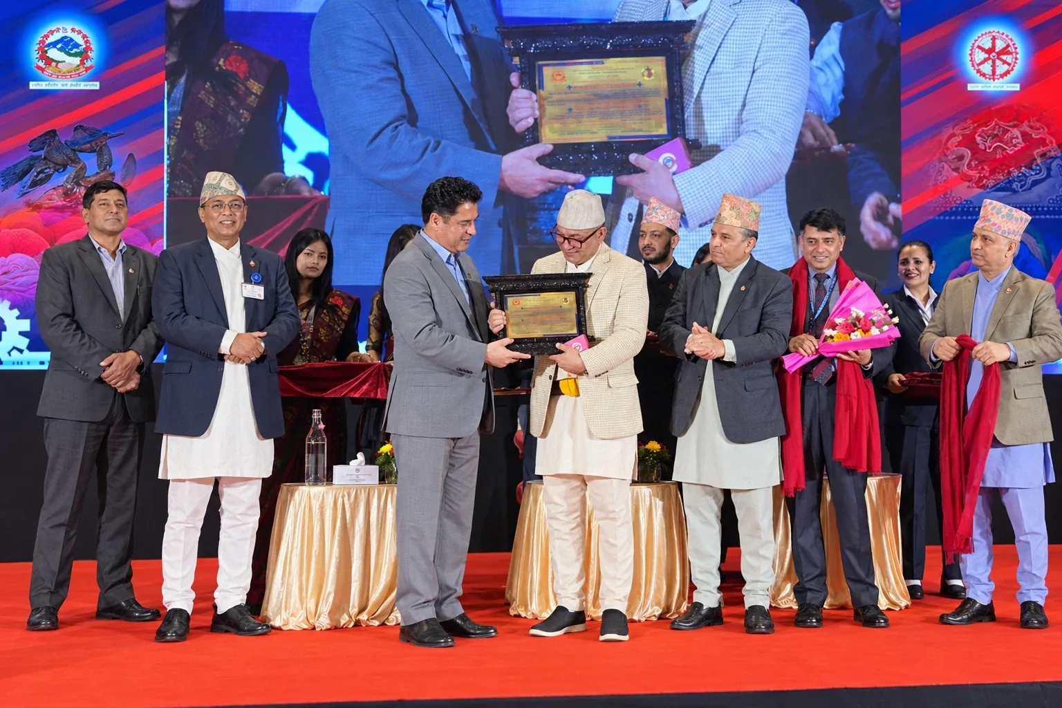On stage at a Government of Nepal ceremony, the Commercially Important Person (CIP) award plaque is handed over as officials look on
