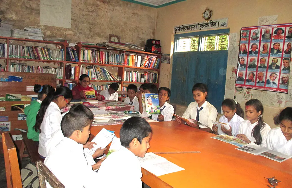 Students reading at tables in a school library lined with full bookshelves